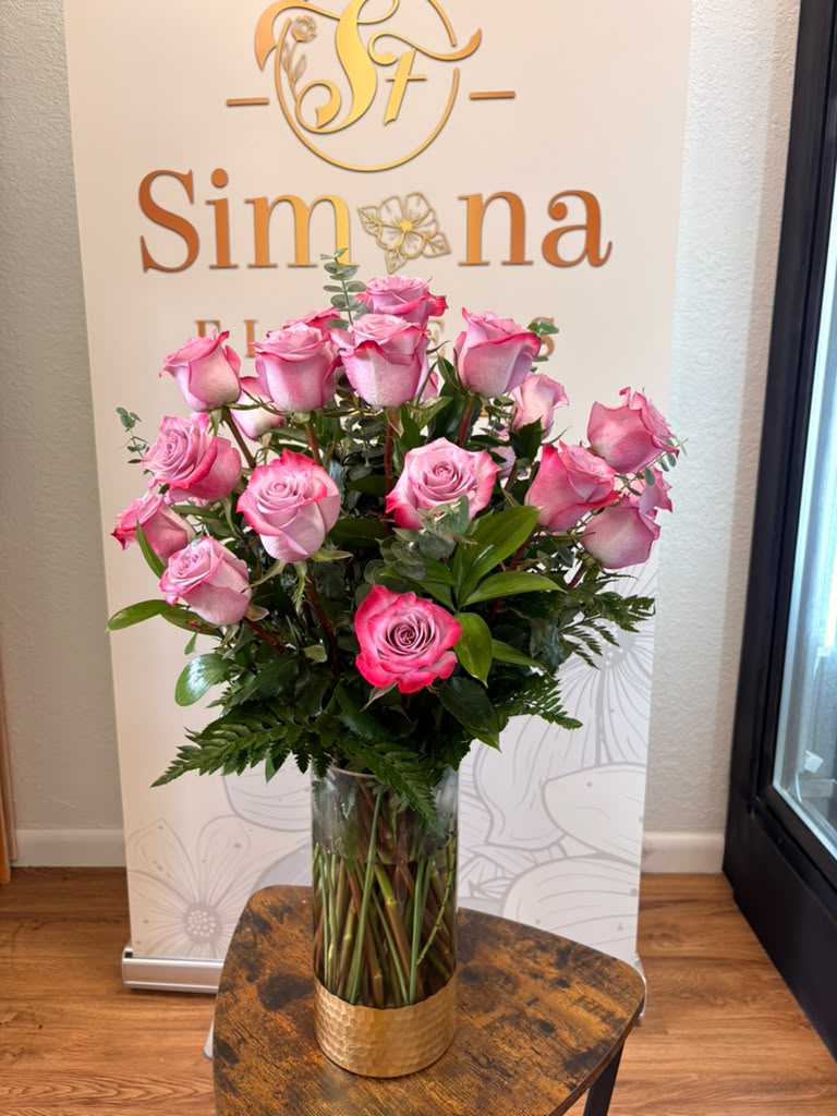 24 lavender roses arranged in a tall glass vase with greenery